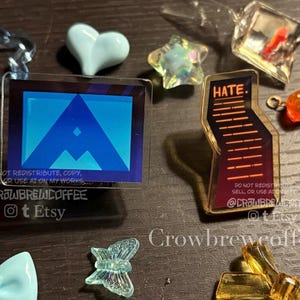May include: A collection of acrylic charms including a rectangular piece with a blue triangle graphic, a tall irregular charm with the text HATE and horizontal lines, plus various star, heart, butterfly, and bow-shaped translucent plastic pieces.