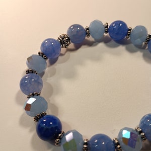 May include: A blue and light blue beaded bracelet with silver accents. The bracelet is made with round and faceted beads.