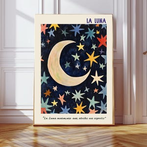 Peut inclure: Impression d'art encadrée avec une lune en croissant et des étoiles colorées sur fond bleu foncé. Le texte "LA LUNA" est en haut, avec une citation française en bas. L'œuvre est exposée dans une pièce avec un plancher en bois.