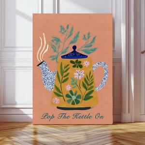 May include: A canvas print depicting a yellow teapot with blue and white patterns, decorated with green leaves and flowers. Steam rises from the spout. The text "Pop The Kettle On" is at the bottom of the image, set against a peach background.
