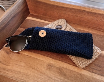 May include: A blue knitted sunglasses case with a wooden button closure. The case is lying on top of a tan knitted case.