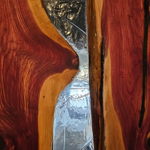 May include: A close-up of a wooden panel with a large, irregular shaped piece of clear glass embedded in it. The wood is a rich reddish-brown color with darker streaks running through it.