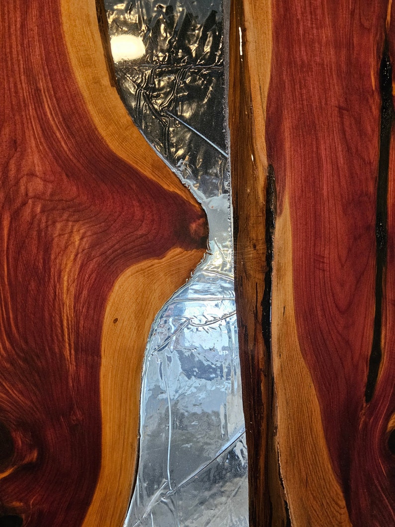 May include: A close-up of a wooden panel with a large, irregular shaped piece of clear glass embedded in it. The wood is a rich reddish-brown color with darker streaks running through it.