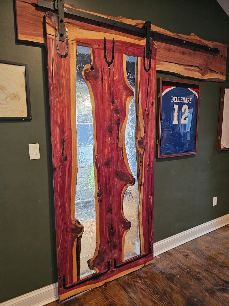 May include: A wooden sliding door with a large glass panel featuring a unique, organic design. The door is made of reddish-brown wood with a natural grain pattern. The glass panel is clear and has a wavy, irregular shape. The door is mounted on a black metal track.