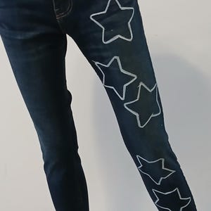 May include: Dark blue denim jeans with white star designs on the right leg.
