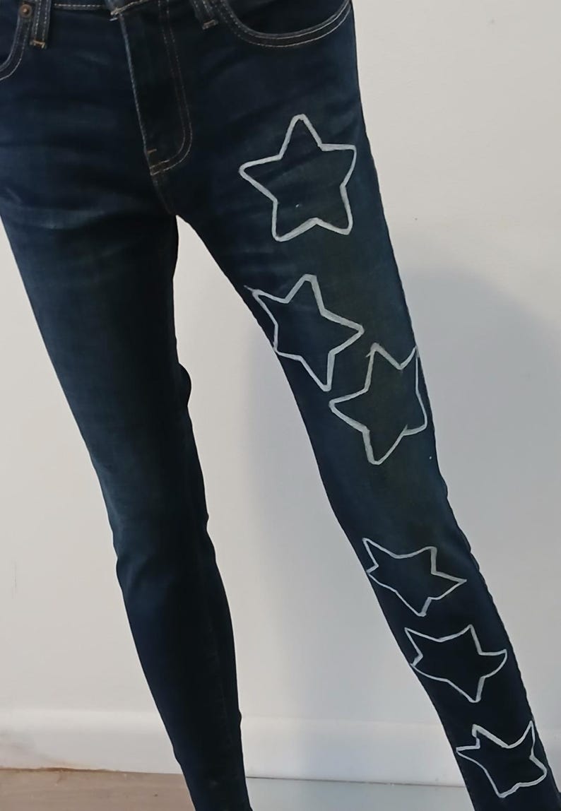 May include: Dark blue denim jeans with white star designs on the right leg.