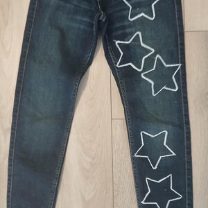 May include: Dark blue denim jeans with five white star shapes sewn on the right leg.