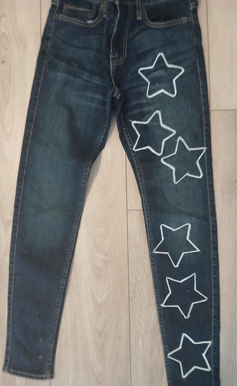 May include: Dark blue denim jeans with five white star shapes sewn on the right leg.