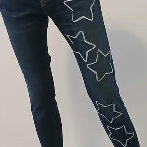 May include: Dark blue denim jeans with white star outlines on the right leg.