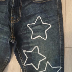 May include: Dark blue denim jeans with three white star shapes outlined on the front of the leg.