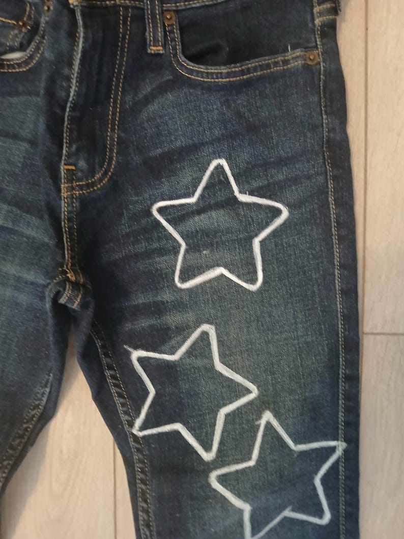 May include: Dark blue denim jeans with three white star shapes outlined on the front of the leg.