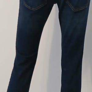 May include: A pair of dark blue denim jeans with a straight leg fit. The jeans have two back pockets with a decorative stitching detail.