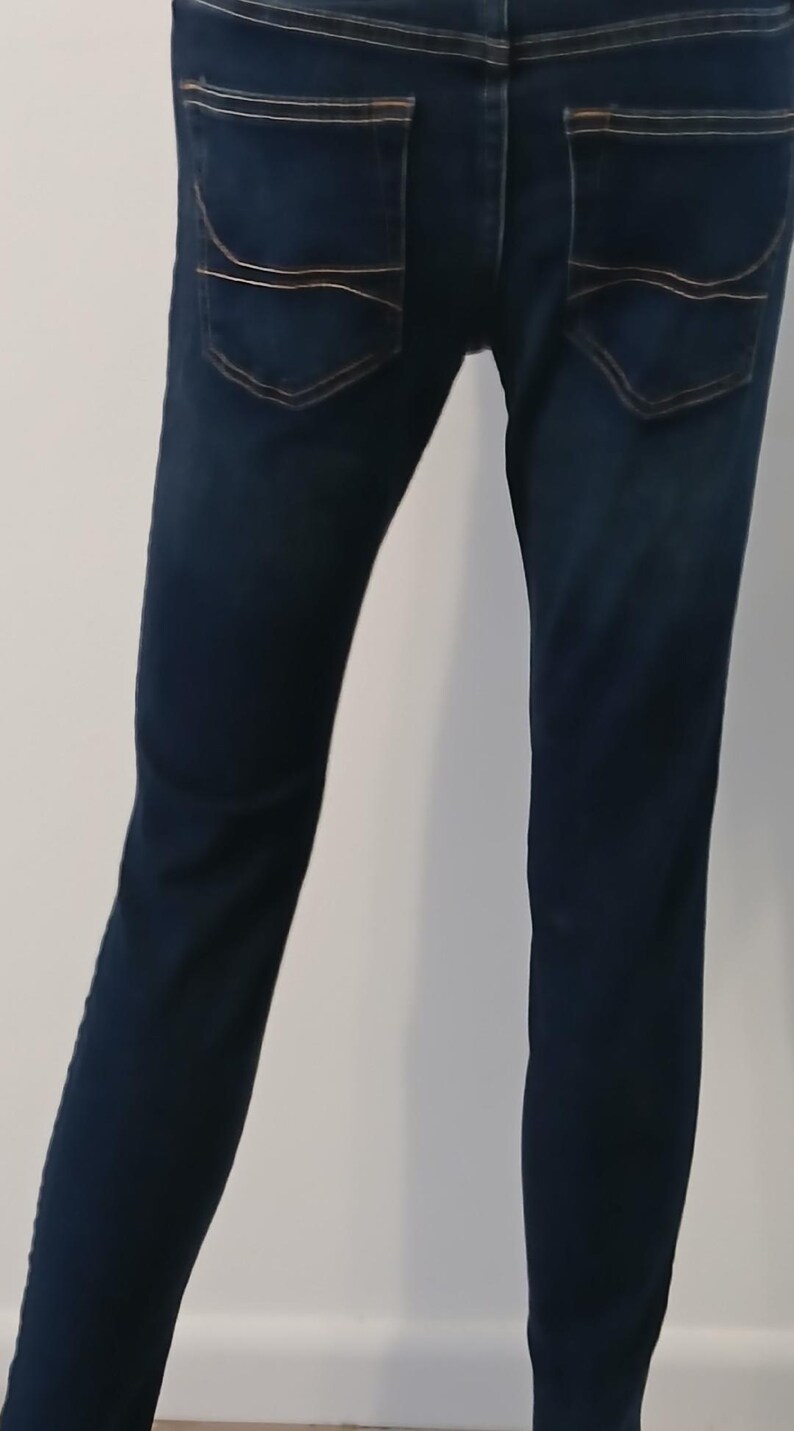 May include: A pair of dark blue denim jeans with a straight leg fit. The jeans have two back pockets with a decorative stitching detail.