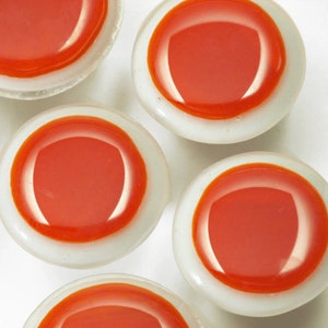 Könnte beinhalten: Fünf runde, weiße Glasknöpfe mit einem leuchtend orangenen Zentrum. Die Knöpfe haben einen erhöhten Rand um das orangefarbene Zentrum.