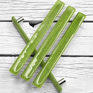 Peut inclure: Trois poignées de porte de placard en verre vert avec un bouton en métal argenté sur chacune. Les poignées sont disposées en forme de croix sur une surface en bois blanc.