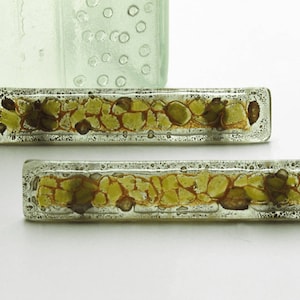 Op de afbeelding: Twee rechthoekige glazen kastknoppen met een textuur, groene en gouden afwerking. De knoppen hebben een verhoogd, getextureerd ontwerp.