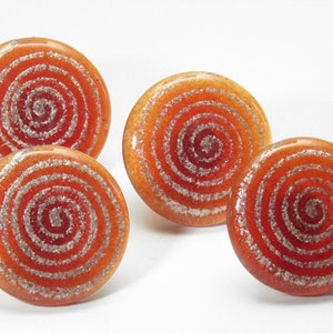 Könnte beinhalten: Vier runde orangefarbene und silberne Glasknöpfe mit einem Spiralmuster.