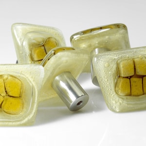 Könnte beinhalten: Vier quadratische Glas-Schrankknöpfe mit einem gelben Glasdesign. Die Knöpfe haben eine silberne Metallbefestigungsschraube.