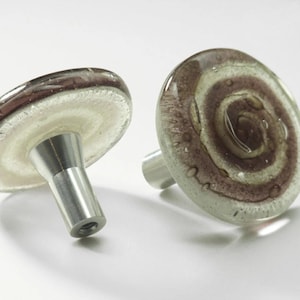 May include: Two glass cabinet knobs with a silver metal base. The glass is clear with a white and purple swirl pattern.