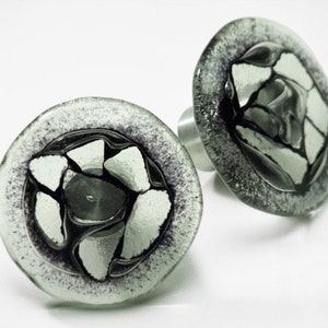 Könnte beinhalten: Zwei runde Glasknöpfe mit einem schwarzen und weißen Mosaikdesign. Die Knöpfe haben eine silberne Metallbasis.