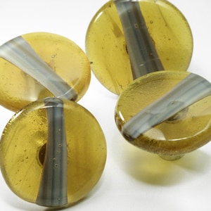 May include: Four round glass knobs with a light brown and gray striped design. The knobs have a shiny finish and are perfect for adding a touch of elegance to any cabinet or drawer.