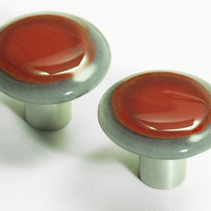 Puede incluir: Dos pomos redondos de vidrio para armario con base plateada. Los pomos tienen un centro rojo y un anillo exterior gris.