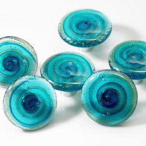 Può includere: Sei pomelli per armadi in vetro blu turchese con un motivo a spirale e dettagli argentati.