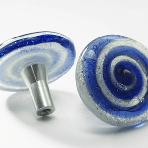 Può includere: Due pomelli per armadi in vetro blu e bianco con una base in metallo argentato. Il vetro è striato di bianco e blu e ha una texture punteggiata.