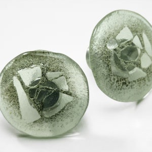 Puede incluir: Un par de pomos redondos de vidrio verde con un diseño geométrico blanco. Los pomos tienen una superficie texturizada y un centro metálico.