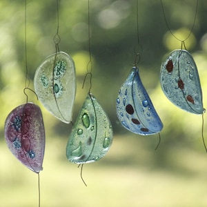Peut inclure: Cinq ornements en verre en forme de feuille suspendus à de fins fils. Les feuilles sont dans des tons de bleu, vert et violet avec des accents blancs et rouges. Les feuilles ont un aspect texturé et bulleux.