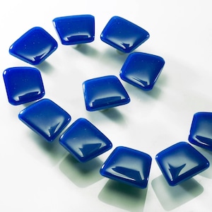 Puede incluir: Un juego de diez pomos de armario de vidrio azul en forma de diamante. Los pomos están dispuestos en una línea curva.