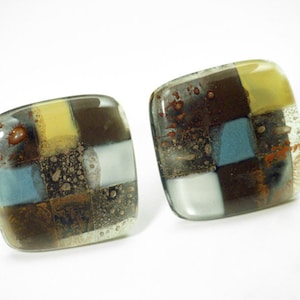 Può includere: Un paio di orecchini quadrati in vetro con un motivo a scacchi in tonalità di marrone, giallo, blu e bianco. Il vetro ha una texture punteggiata.