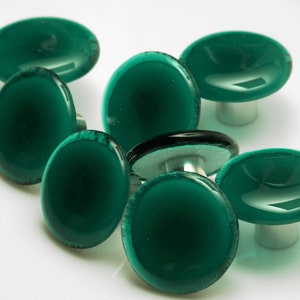 Puede incluir: Siete pomos de armario de vidrio verde azulado con base plateada. Los pomos son redondos y tienen una ligera hendidura en el centro.