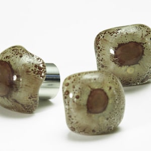 May include: Three square-shaped glass knobs with a brown and white marbled design. The knobs have a metallic silver base.