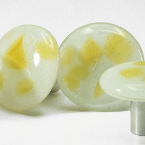 Può includere: Una collezione di oggetti decorativi a forma di fungo in vetro. I funghi hanno una base bianca con accenti gialli. Alcuni sono rotondi, altri ovali o a forma di fungo. Gli steli sono color argento.