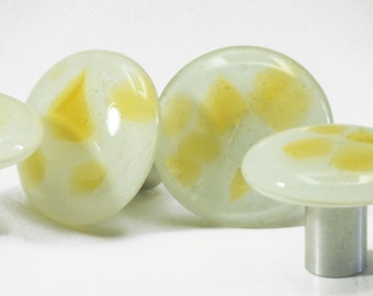 Könnte beinhalten: Eine Sammlung dekorativer pilzförmiger Objekte aus Glas. Die Pilze haben eine weiße Basis mit gelben Akzenten. Einige sind rund, andere oval oder pilzförmig. Die Stiele sind silberfarben.