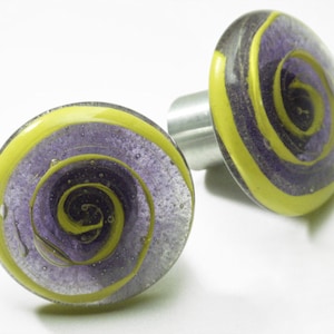 May include: Two round glass knobs with a yellow and purple swirl design. The knobs have a silver metal base.