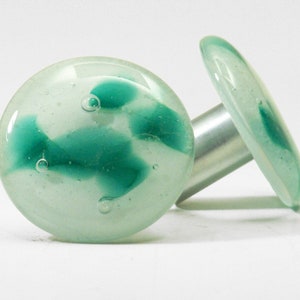 May include: Two round glass knobs with a white background and green swirls. The knobs are attached to a silver metal post.