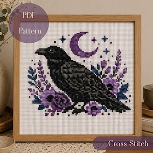 May include: A cross stitch pattern in a wooden frame featuring a black raven centered among purple flowers and foliage. Above the bird is a purple crescent moon and small blue stars. The text PDF Pattern is visible in the upper left corner.