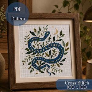 May include: A cross stitch pattern featuring a blue snake coiled among green foliage and small gold stars, with a crescent moon above. The design is displayed in a square wooden frame. The text PDF Pattern and Cross Stitch 100 x 100 appear.