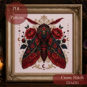 May include: A cross stitch pattern featuring a moth with dark blue and red wings adorned with red roses, set against a light fabric background. The design includes small crescent moon symbols and decorative flourishes, all encased in an ornate gold frame.