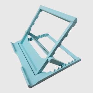 May include: A light blue wooden book stand. The stand is adjustable and features a sloped surface to hold a book. The stand has a rectangular base and a frame with notches to adjust the angle. The stand is made of wood.