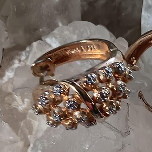 May include: Close-up of a gold-toned earring with a cluster of small, sparkling stones. The earring has a curved design with a hinged closure. The text "Tiffany & Co. 925" is visible on the inside of the earring.