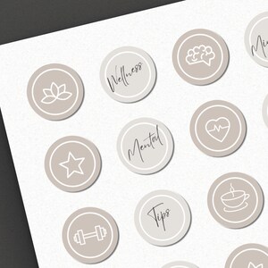 Op de afbeelding: Een set van 12 beige ronde social media-iconen met witte contouren en zwarte tekst. De iconen bevatten verschillende wellness-gerelateerde symbolen, waaronder een lotusbloem, een brein, een hart met een hartslag, een ster, een halter, een kopje thee en de woorden "Wellness", "Mindful", "Zorg voor jezelf", "Mentaal", "Tips" en "Gezondheid".