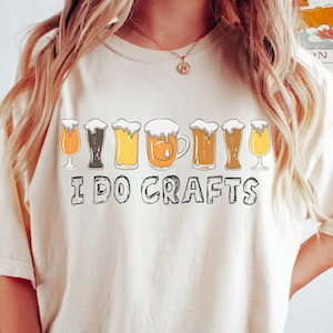 Può includere: Una maglietta beige con una grafica di una fila di bicchieri di birra e il testo "I DO CRAFTS".