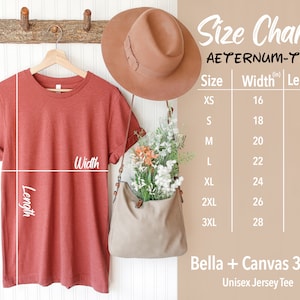 May include: A rust-colored Bella + Canvas 3001 Unisex Jersey Tee hangs on a wooden rack. A size chart displays measurements in inches, with sizes ranging from XS to 3XL. The chart includes the text "AETERNUM-TEE". A brown hat and a beige bag with flowers are also visible.