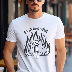 May include: White t-shirt with a black and white illustration of a stick figure standing in front of flames. The text "EVERYTHING IS FINE" is above the figure.