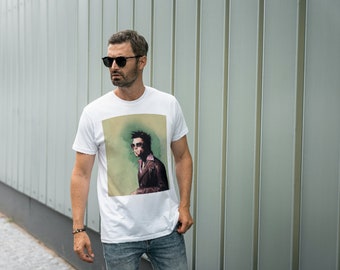 Könnte beinhalten: Ein weißes T-Shirt mit einem Grafikdruck eines Mannes mit Sonnenbrille und Lederjacke. Die Grafik ist im Vintage-Stil mit grünem und braunem Hintergrund.