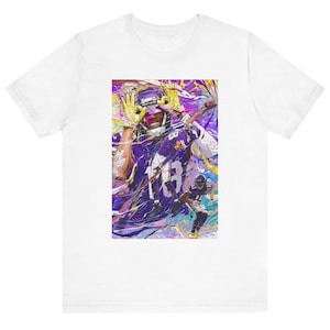 May include: White t-shirt featuring a vibrant graphic of a football player in a purple and gold uniform. The artwork has a dynamic, abstract style with splashes of color. The player is in action, with a football in hand.
