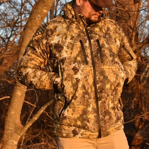 May include: A camouflage jacket with a zipper closure and a hood. The jacket has a pattern of brown, green, and white.